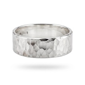 A single, wide, hammered silver band ring with a slightly irregular edge is shown on a white background, casting a shadow.