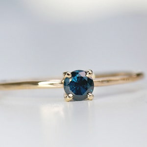Puede incluir: Un anillo de oro con una piedra preciosa de diamante azul engastada en un engaste de cuatro garras.