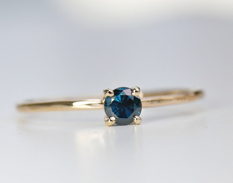 Puede incluir: Un anillo de oro con una piedra preciosa de diamante azul engastada en un engaste de cuatro garras.