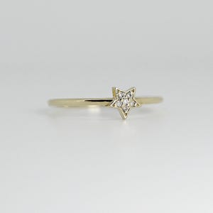 A thin gold ring with a small star shape on top, encrusted with tiny diamonds, is centered on a white background, viewed from a slightly different angle.