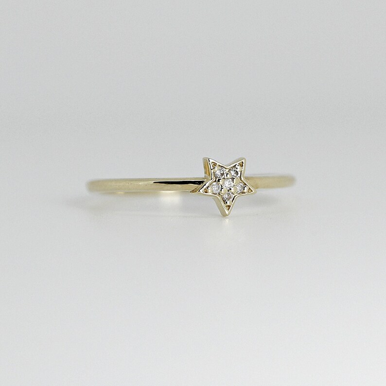 A thin gold ring with a small star shape on top, encrusted with tiny diamonds, is centered on a white background, viewed from a slightly different angle.