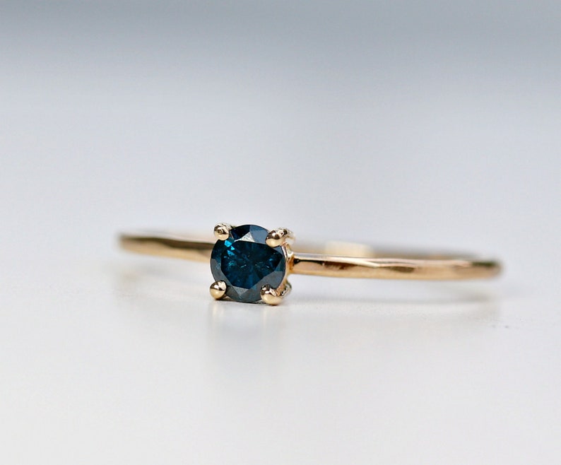 Puede incluir: Un anillo de oro con una piedra preciosa azul oscuro engastada en un engaste de cuatro garras.