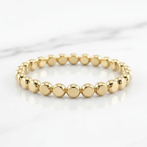 May include: A gold beaded bracelet. The bracelet features a series of small, round, gold beads strung together to form a continuous loop. The beads are evenly spaced and have a polished, reflective surface. The bracelet is displayed on a white marble surface.