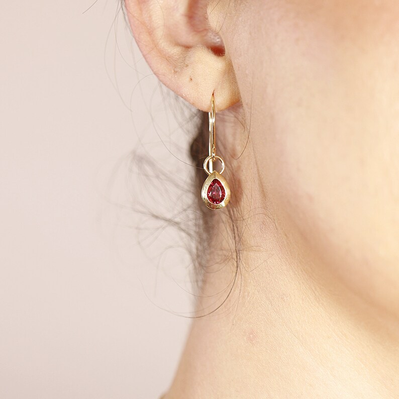 May include: Gold dangle earrings with a small red teardrop-shaped gemstone.