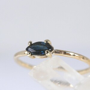 A close-up of a gold ring with a dark blue marquise-cut sapphre showing the hammered texture of the band.