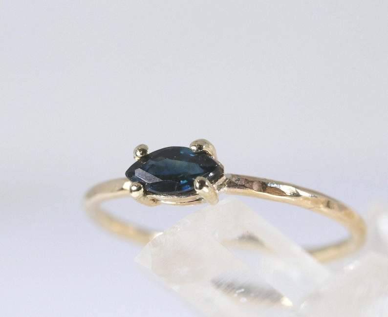 A close-up of a gold ring with a dark blue marquise-cut sapphre showing the hammered texture of the band.