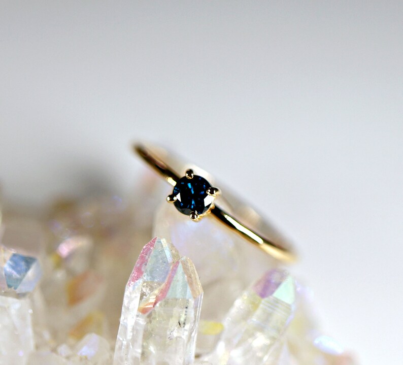 Puede incluir: Un anillo de oro con una sola piedra preciosa redonda de color azul oscuro engastada en un engaste de cuatro garras.