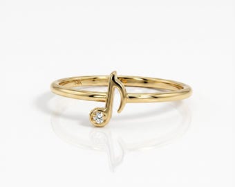Può includere: Un anello d'oro con un motivo a forma di nota musicale e un piccolo diamante. L'anello è in oro lucido e ha una fascia delicata. La nota musicale è una chiave di violino con un diamante alla base.