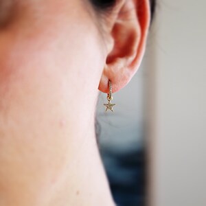 May include: A gold hoop earring with a small star charm dangling from it. The star is also set with small diamonds.