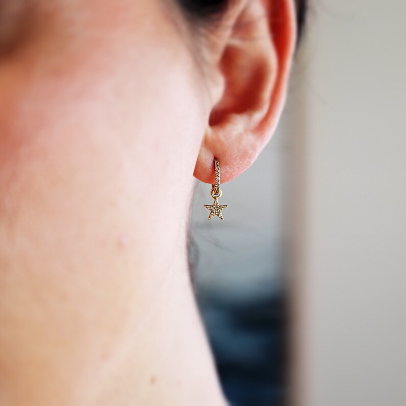 May include: A gold hoop earring with a small star charm dangling from it. The star is also set with small diamonds.