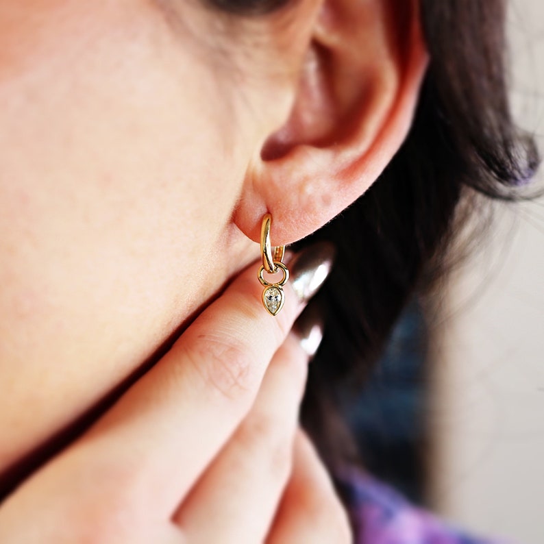 May include: Gold hoop earrings with a small teardrop-shaped diamond dangling from each hoop.