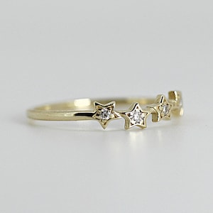 A gold ring with five diamond-studded stars, viewed from a slight angle on a white surface.