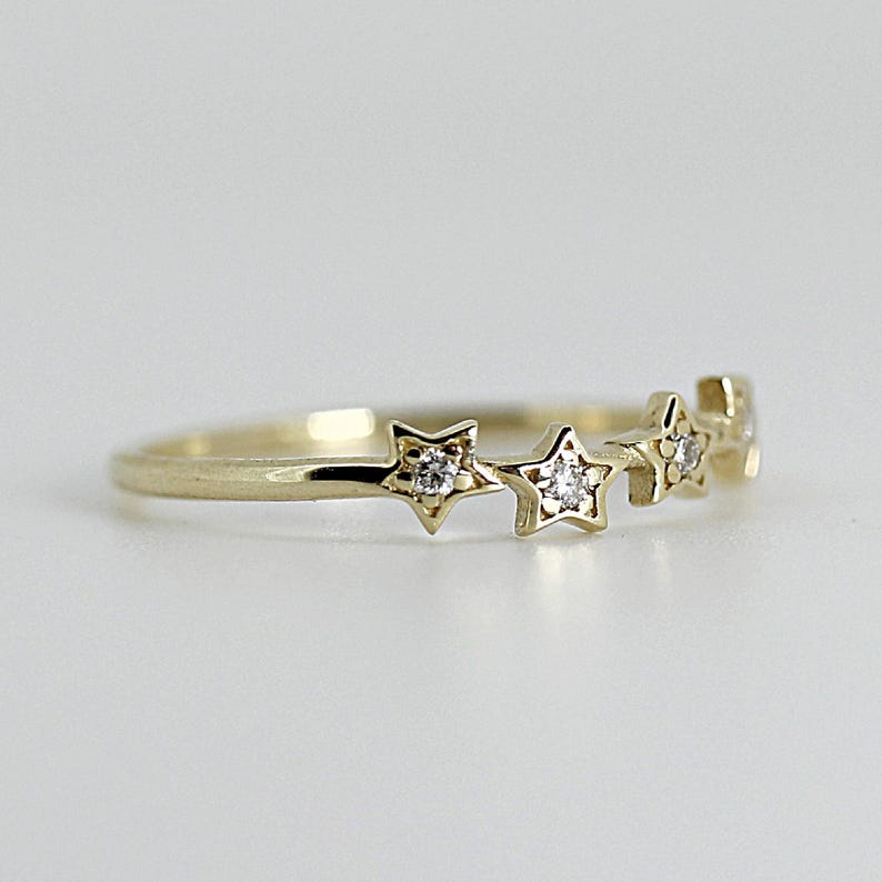 A gold ring with five diamond-studded stars, viewed from a slight angle on a white surface.