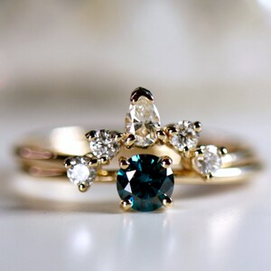 Puede incluir: Un anillo de oro con una piedra preciosa azul rodeada de piedras blancas m&aacute;s peque&ntilde;as. El anillo est&aacute; colocado sobre una superficie blanca.