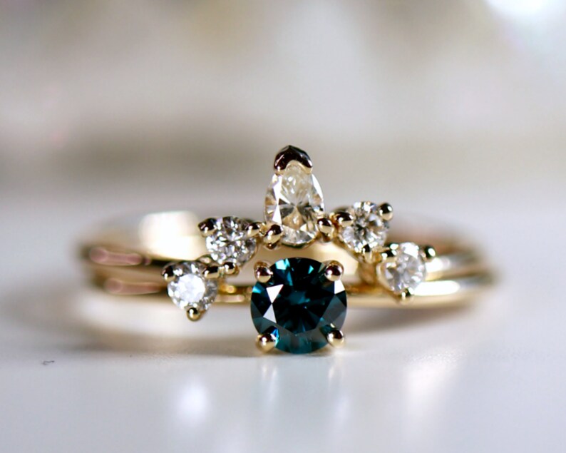 Puede incluir: Un anillo de oro con una piedra preciosa azul rodeada de piedras blancas m&aacute;s peque&ntilde;as. El anillo est&aacute; colocado sobre una superficie blanca.