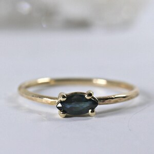 A gold ring with a dark blue marquise-cut sapphire set horizontally, viewed from slightly above against a white background.