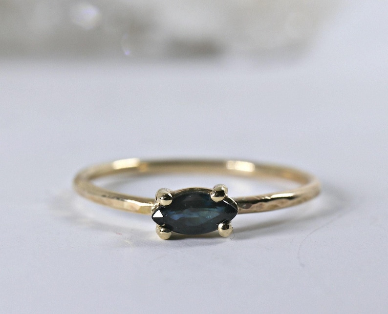 A gold ring with a dark blue marquise-cut sapphire set horizontally, viewed from slightly above against a white background.