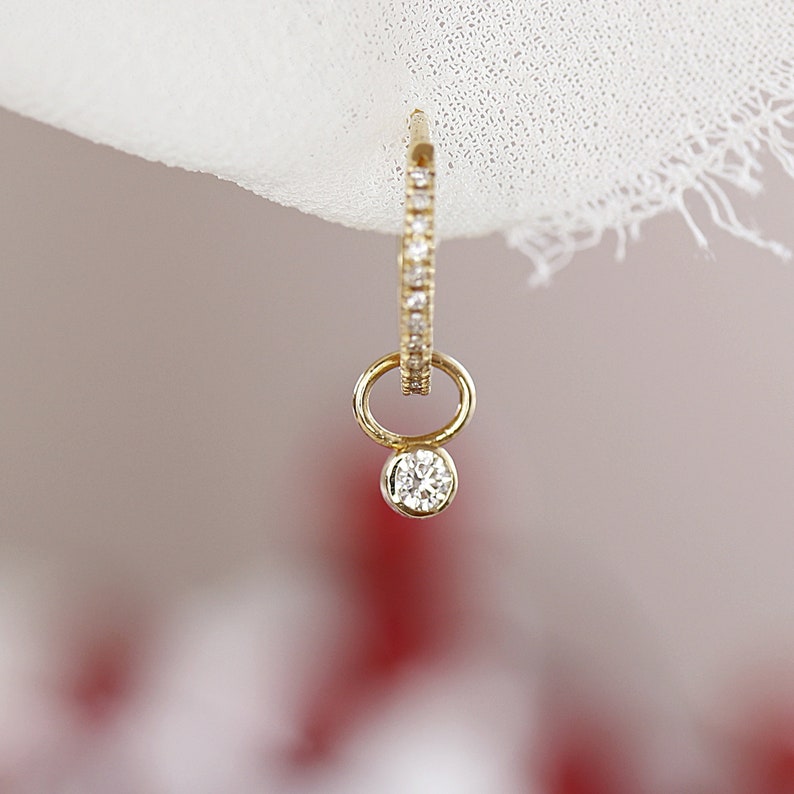 May include: A gold hoop earring with a small diamond dangling from the bottom. The hoop is set with small diamonds.