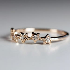 A rose gold ring with five diamond-studded stars across the top, on a white surface.