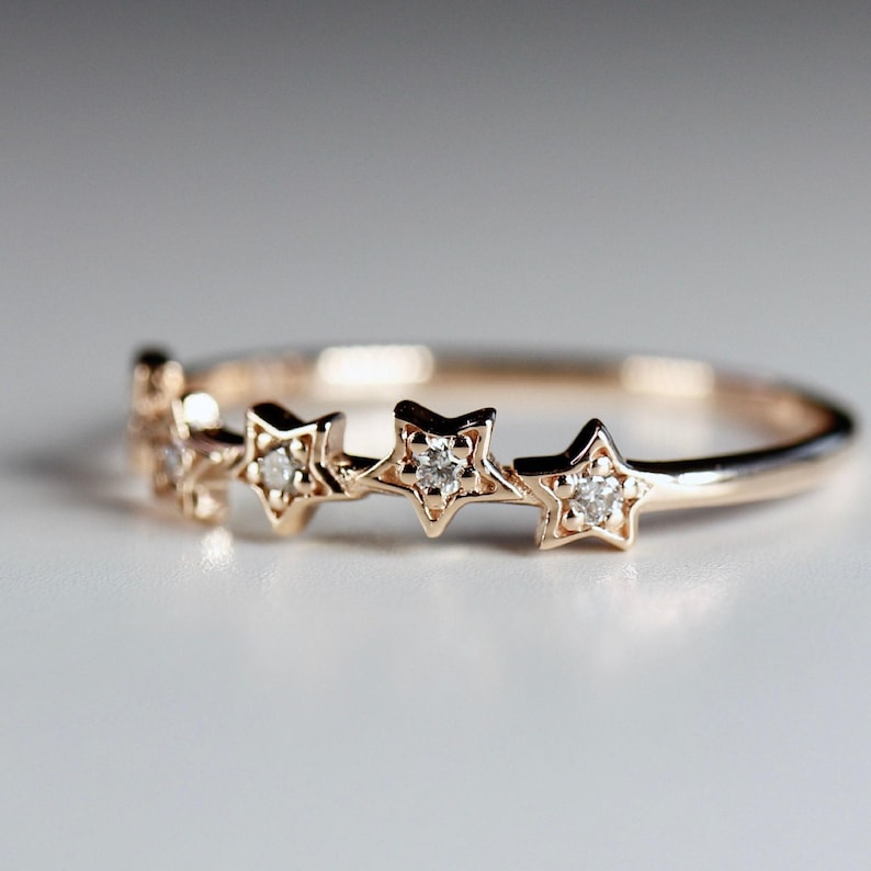 A rose gold ring with five diamond-studded stars across the top, on a white surface.