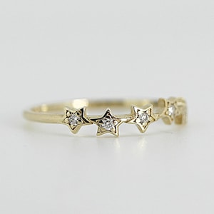 A gold ring with five diamond-studded stars, centered on a white surface.