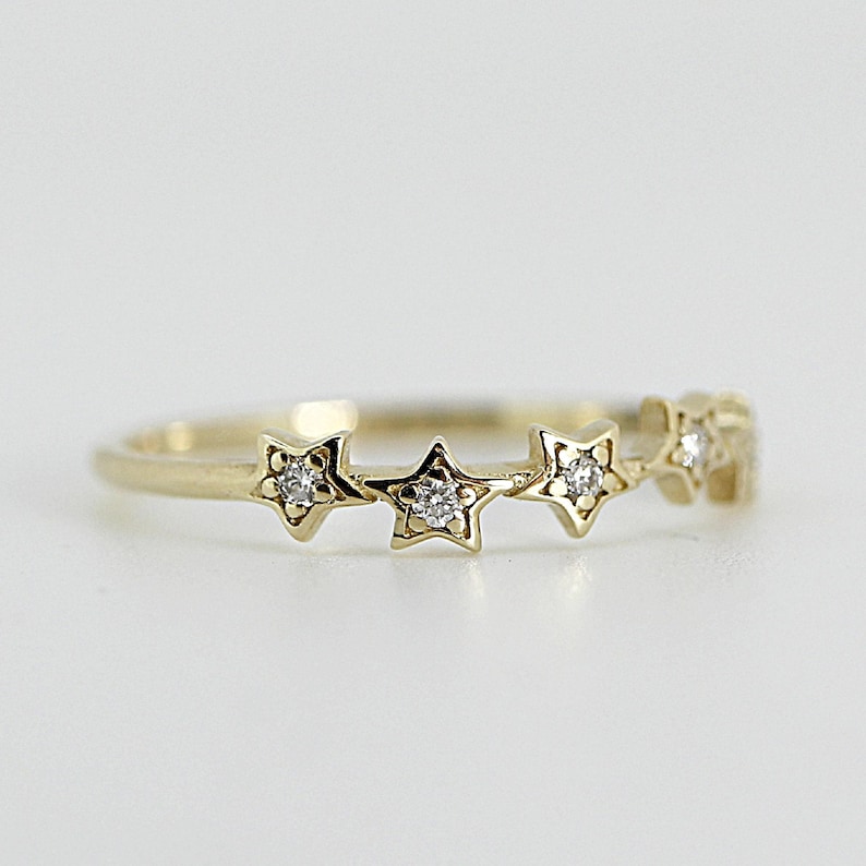 A gold ring with five diamond-studded stars, centered on a white surface.