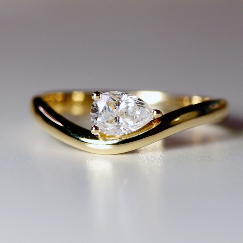 Pode incluir: Um anel de noivado de ouro com um diamante em forma de p&ecirc;ra e um design curvo.