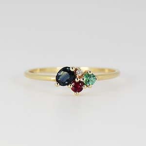 May include: A gold ring with a cluster of colorful gemstones. The ring features a blue sapphire, a red ruby, and two green emeralds.