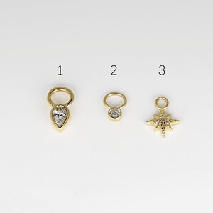 May include: Three gold charms with clear crystal accents. The first charm is a teardrop shape, the second is a round circle, and the third is a star shape.