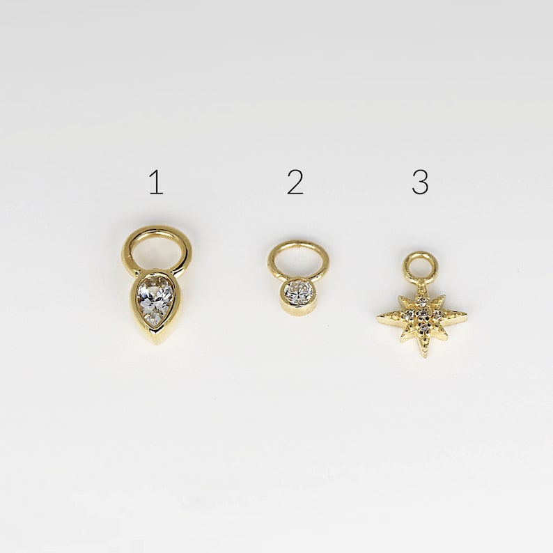 May include: Three gold charms with clear crystal accents. The first charm is a teardrop shape, the second is a round circle, and the third is a star shape.