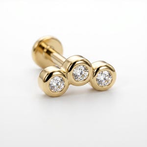 May include: A gold-colored earring with three clear, round gemstones. The earring has a post and a flat back. The gemstones are set in individual bezels, creating a cluster design. The earring is on a white background.