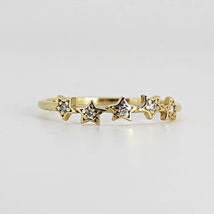 A gold ring with five diamond-studded stars, viewed from directly above on a white surface.
