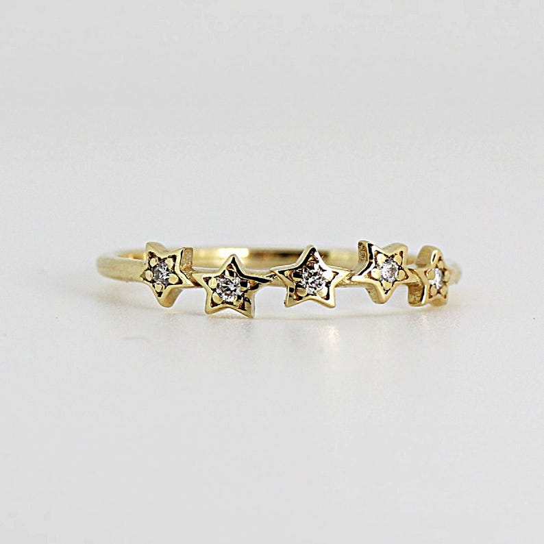 A gold ring with five diamond-studded stars, viewed from directly above on a white surface.