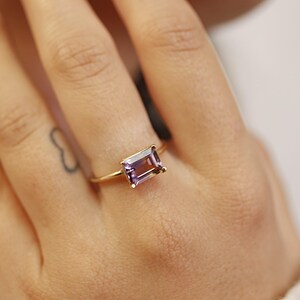 A close-up of a person wearing an emerald-cut ametrine gemstone ring on their ring finger.