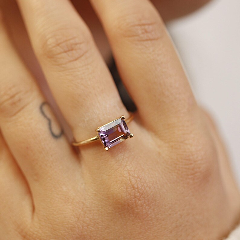 A close-up of a person wearing an emerald-cut ametrine gemstone ring on their ring finger.
