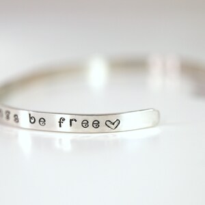 May include: Silver bangle bracelet with the words "things be free" and a heart symbol engraved on it.