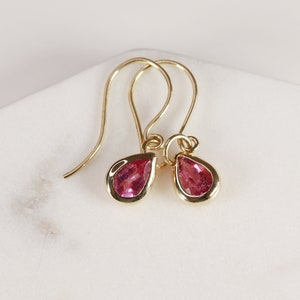 May include: A pair of gold earrings with pink teardrop-shaped gemstones.