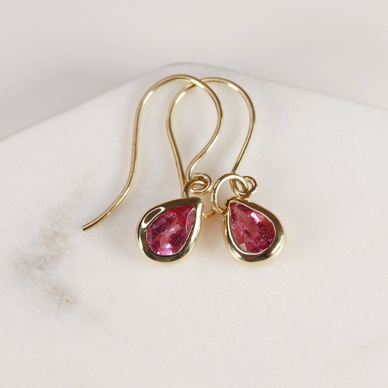 May include: A pair of gold earrings with pink teardrop-shaped gemstones.