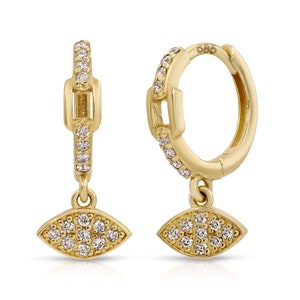 May include: Gold hoop earrings with a dangling evil eye charm. Both the hoop and the charm are adorned with small, clear cubic zirconia stones.