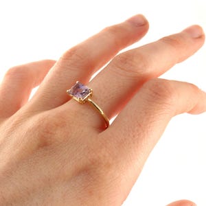 A hand displaying a yellow gold ring with a rectangular purple ametrine gemstone.