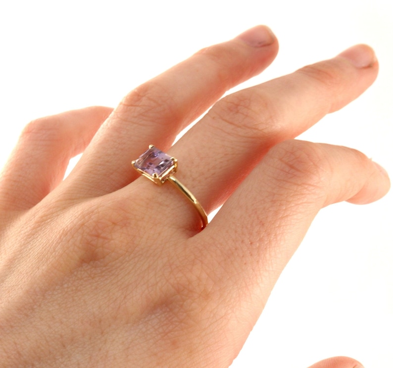 A hand displaying a yellow gold ring with a rectangular purple ametrine gemstone.