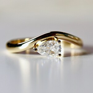 Pode incluir: Um anel de noivado de ouro com um diamante em forma de p&ecirc;ra e um design curvo.