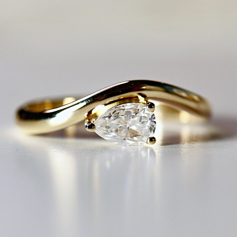 Pode incluir: Um anel de noivado de ouro com um diamante em forma de p&ecirc;ra e um design curvo.