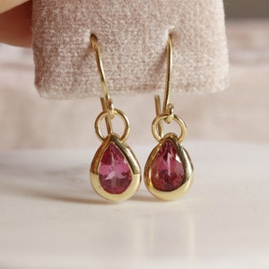 May include: A pair of gold teardrop earrings with pink gemstones.