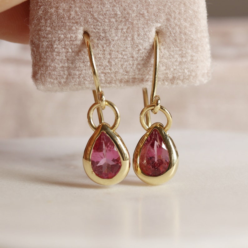 May include: A pair of gold teardrop earrings with pink gemstones.