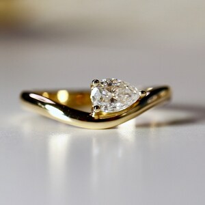 Pode incluir: Uma alian&ccedil;a de noivado de ouro com um diamante em forma de p&ecirc;ra engastado em uma banda curva.