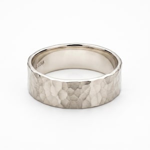 May include: A silver ring with a hammered texture. The ring has a wide band and a textured surface, creating a unique and eye-catching design. The ring is set against a white background.