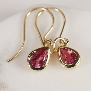 May include: A pair of gold dangle earrings with pink teardrop-shaped gemstones.