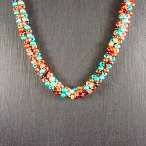 May include: A multi-strand necklace made of small, colorful beads. The beads are in shades of brown, orange, teal, and green. The necklace is arranged in a spiral pattern.
