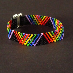 May include: A colorful beaded bracelet with a black background and a silver clasp. The beads are arranged in a chevron pattern, creating a rainbow effect.